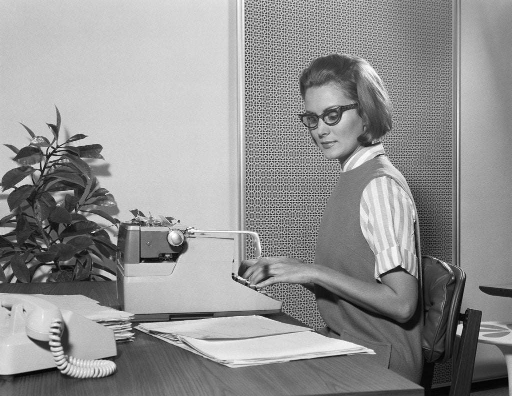 Detail of Secretary typist wearing stylish eyeglasses using manual typewriter at desk by Corbis