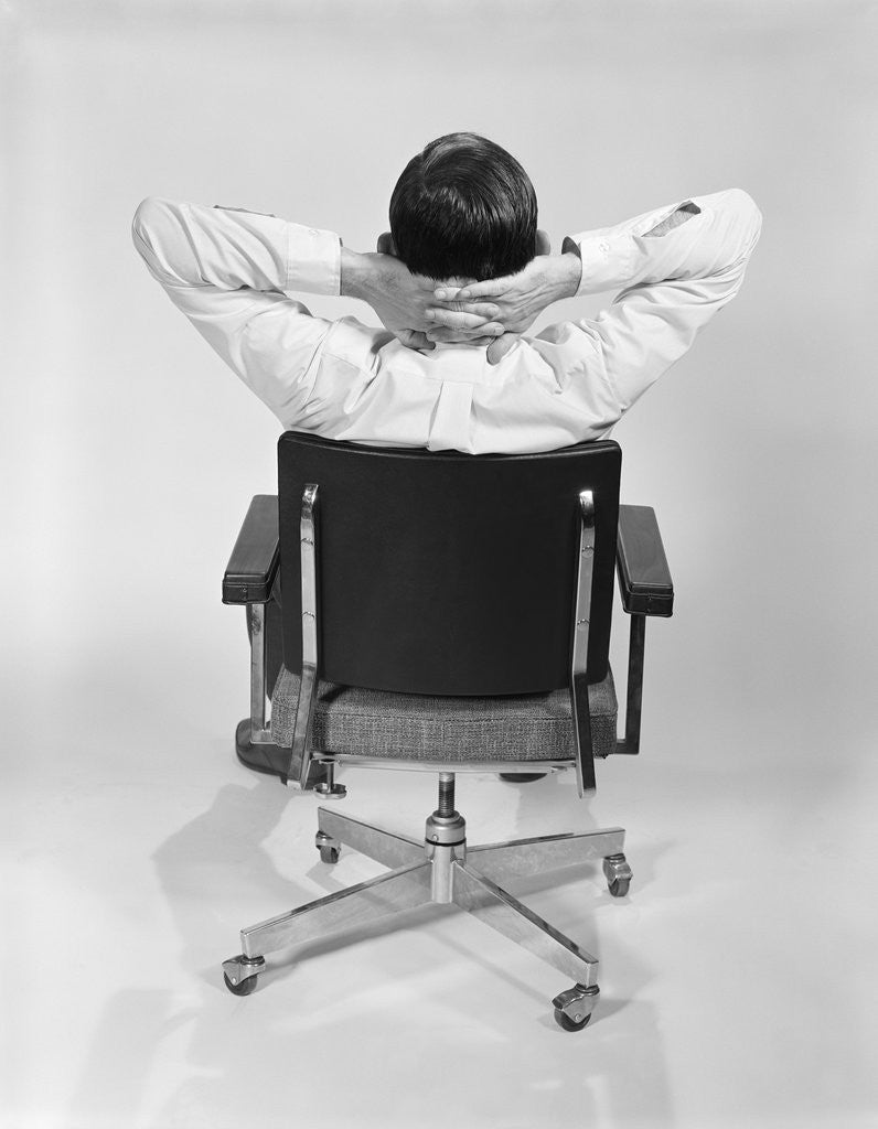 Detail of Man from behind sitting in office executive chair hands clasped behind neck by Corbis