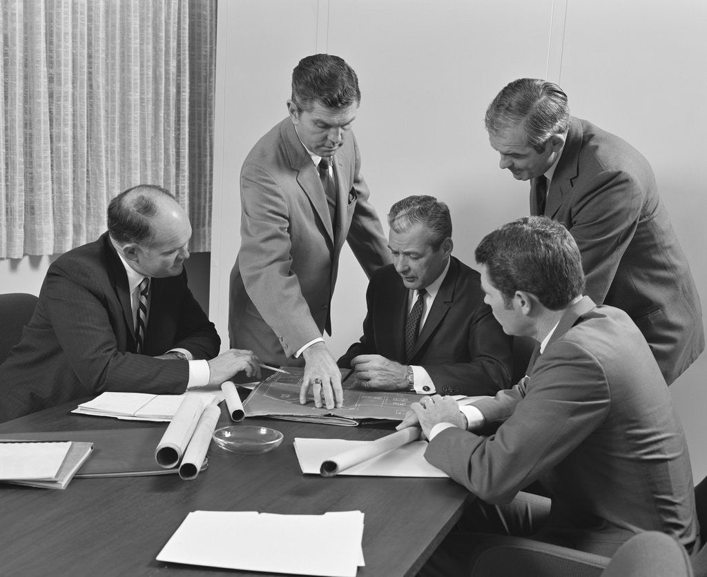 Detail of 5 executive businessmen at conference table meeting looking over papers & blueprints by Anonymous