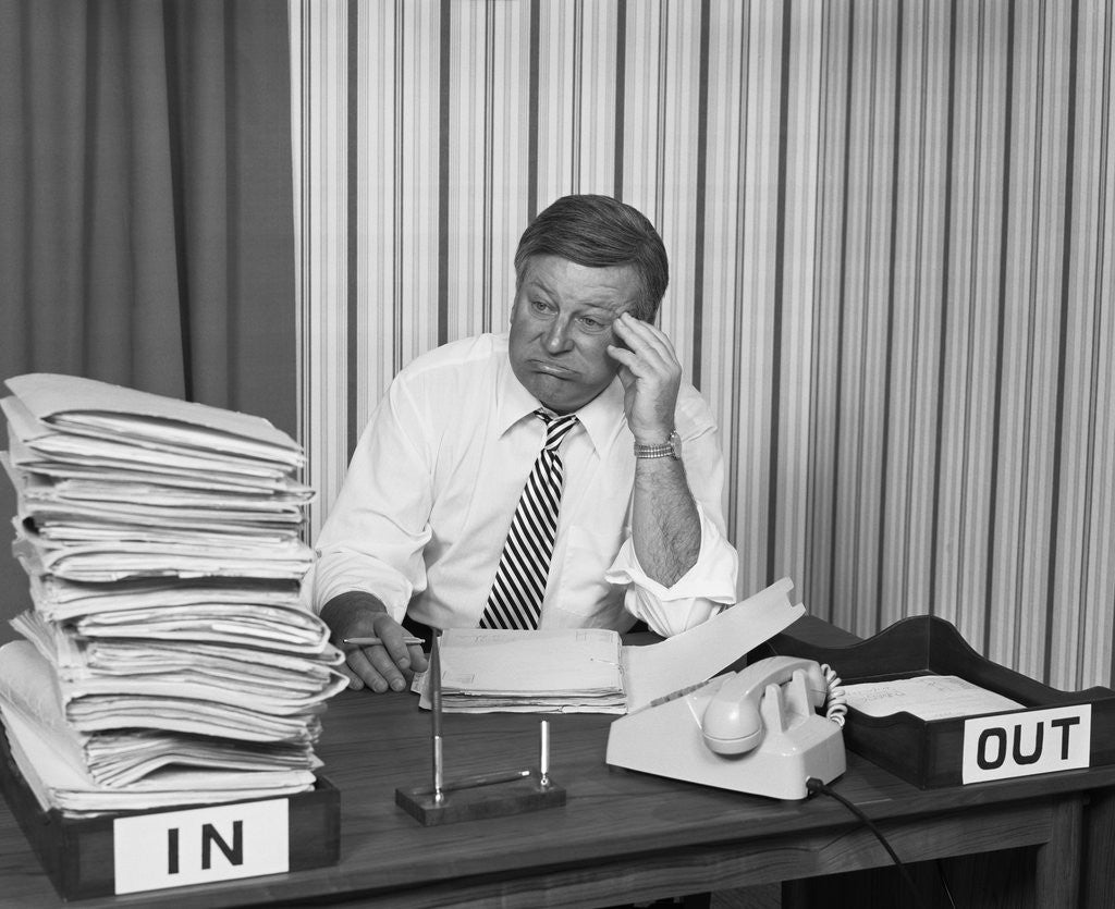 Detail of Concerned businessman staring large pile paperwork in in-box by Anonymous