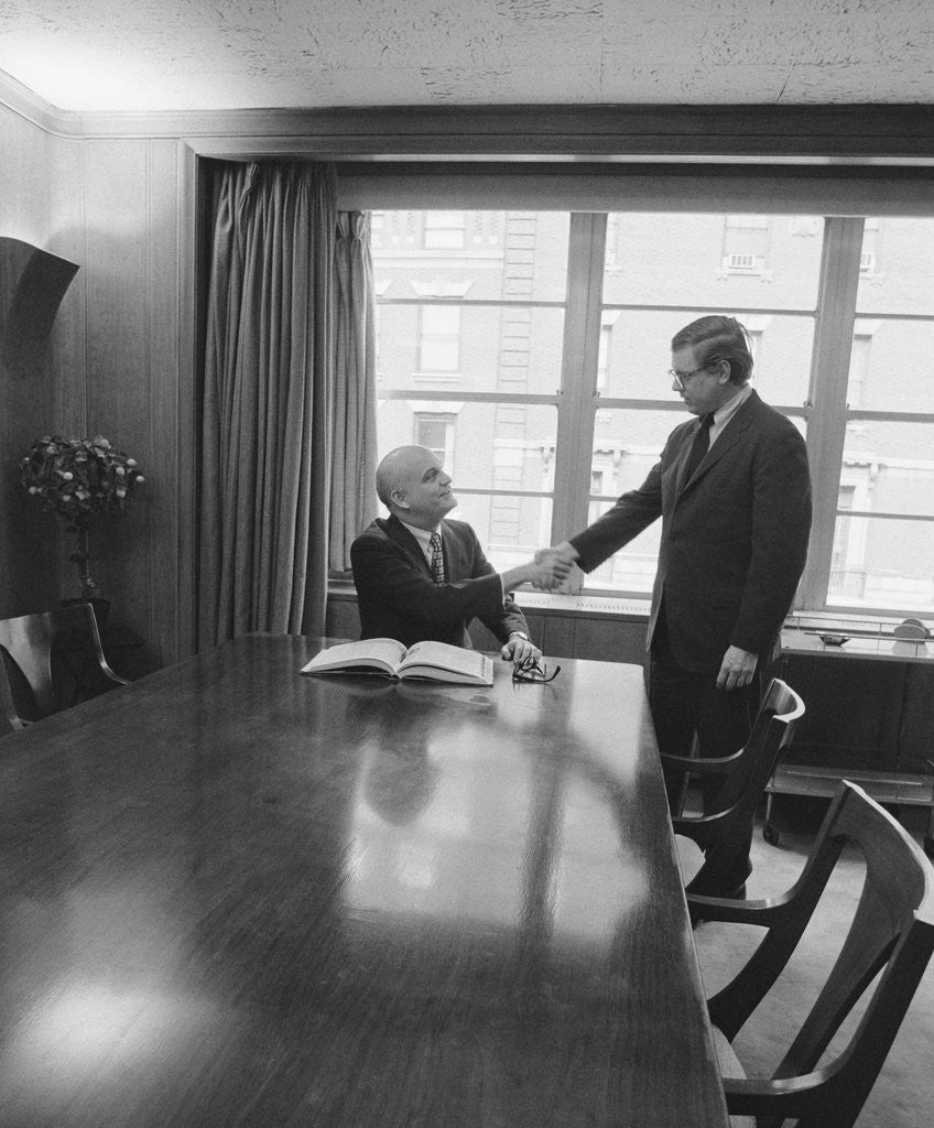 Detail of Two men one seated shaking hands long wooden conference table by Anonymous