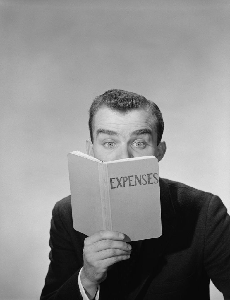 Detail of Man wide open eyes looking into expenses book hiding his lower face by Corbis