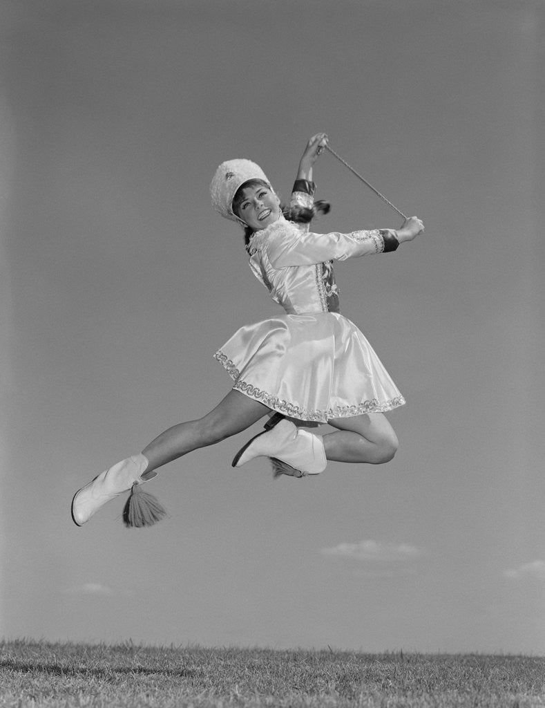 Detail of Woman majorette wearing band uniform holding baton jumping into the air by Anonymous
