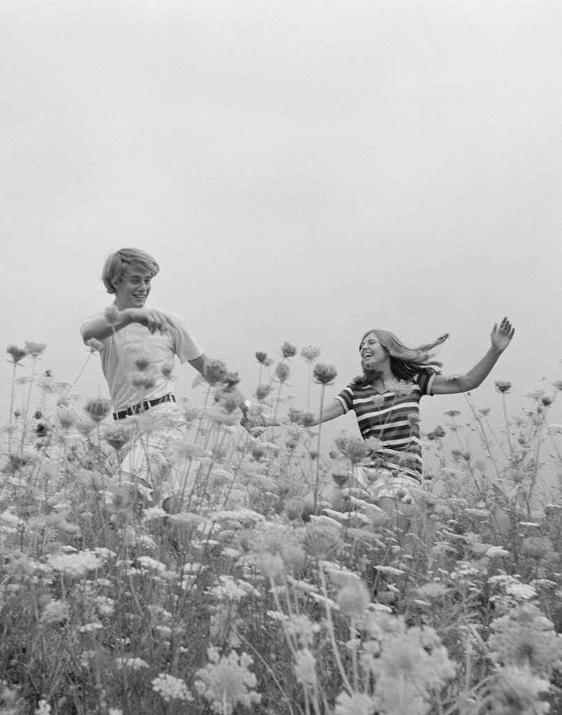 Detail of Young couple holding hands running through field of flowers by Corbis