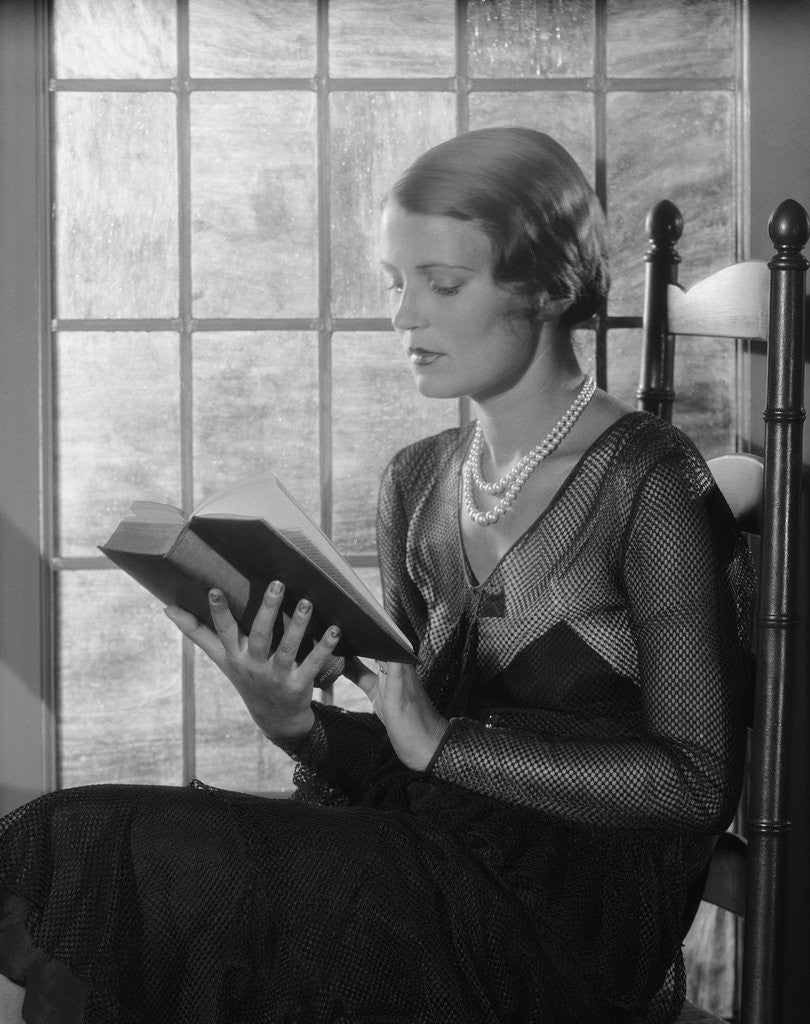 Detail of Elegant woman wearing pearls sitting by window reading book by Anonymous