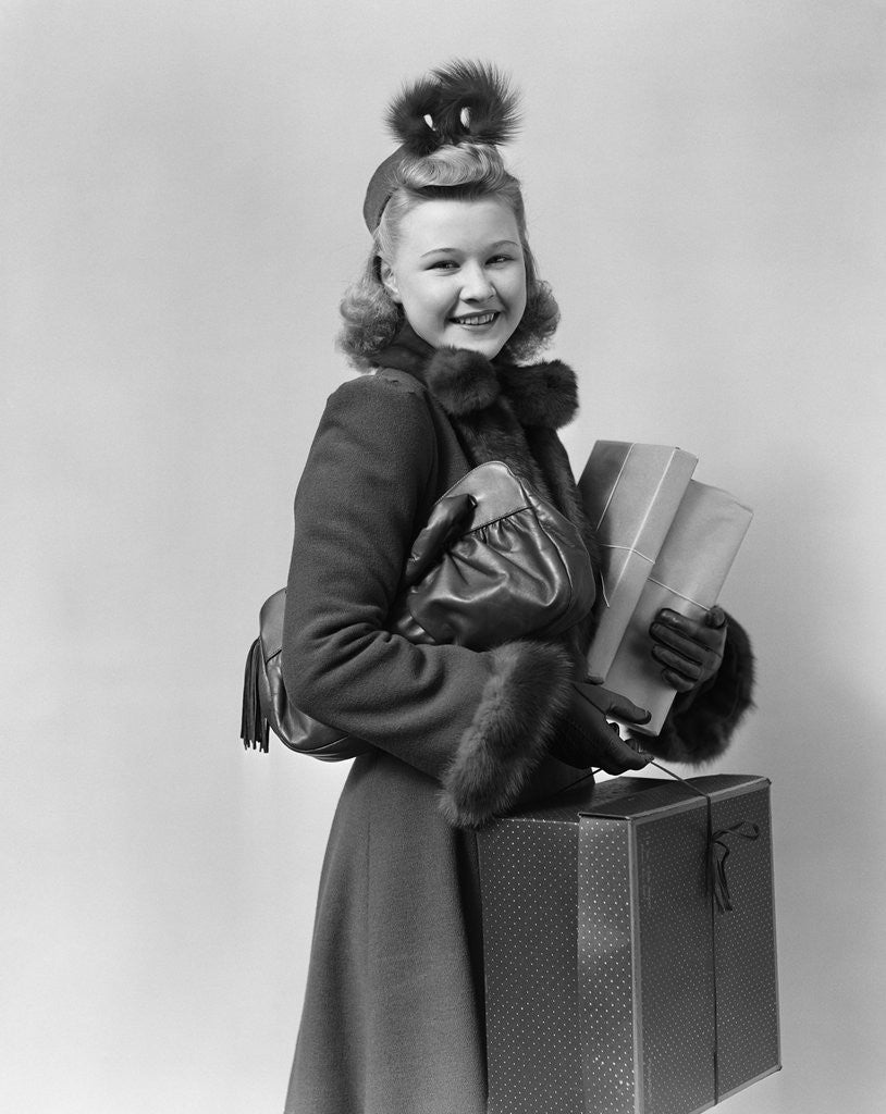 Detail of Smiling young blond woman wearing hat fur trimmed coat carrying packages by Corbis
