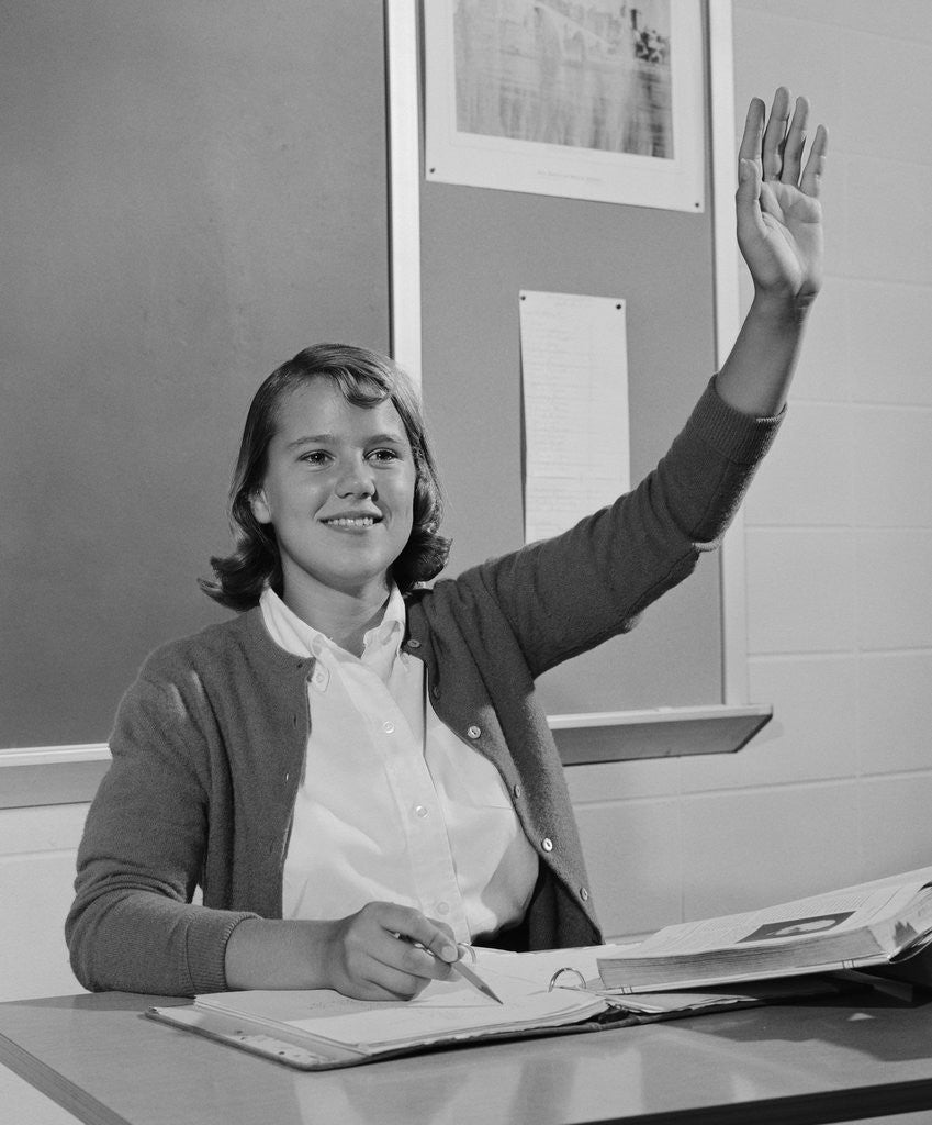 Detail of Smiling teen girl sitting classroom desk raising her hand by Corbis