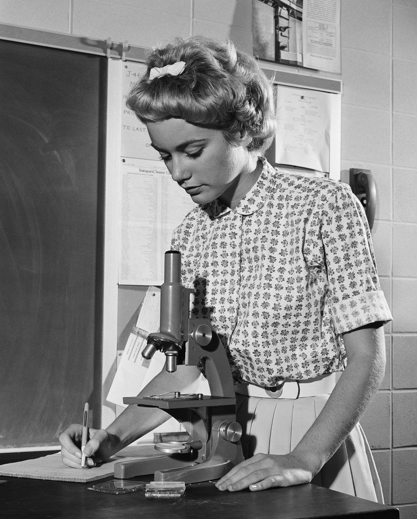 Detail of Teen girl writing notes working with microscope in science classroom by Anonymous