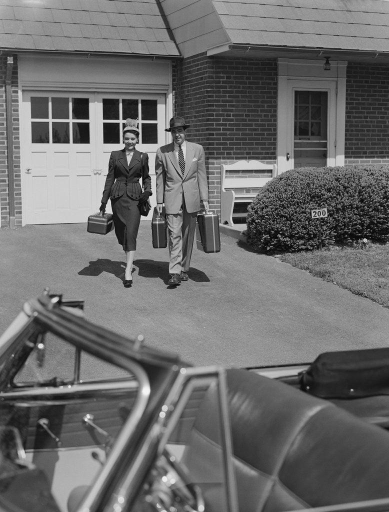 Detail of Couple carrying luggage walking towards convertible car in driveway by Anonymous