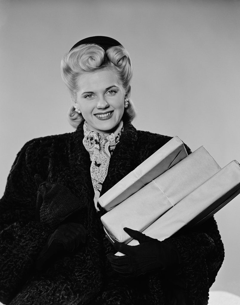 Detail of Blond woman smiling wearing winter coat carrying shopping parcel by Anonymous