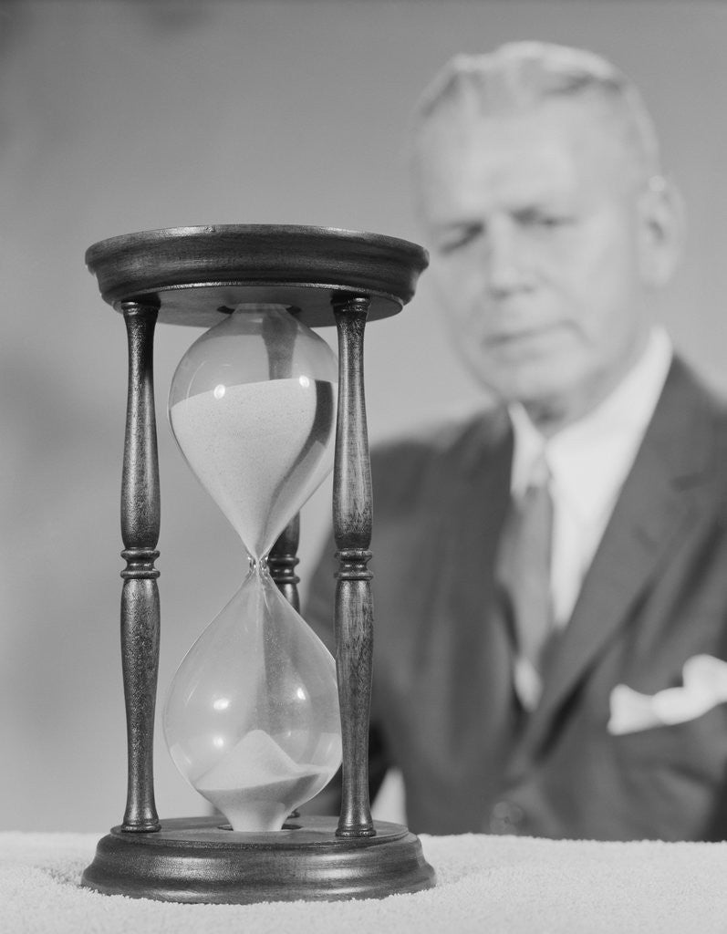 Detail of Elderly man soft focus behind hourglass by Anonymous