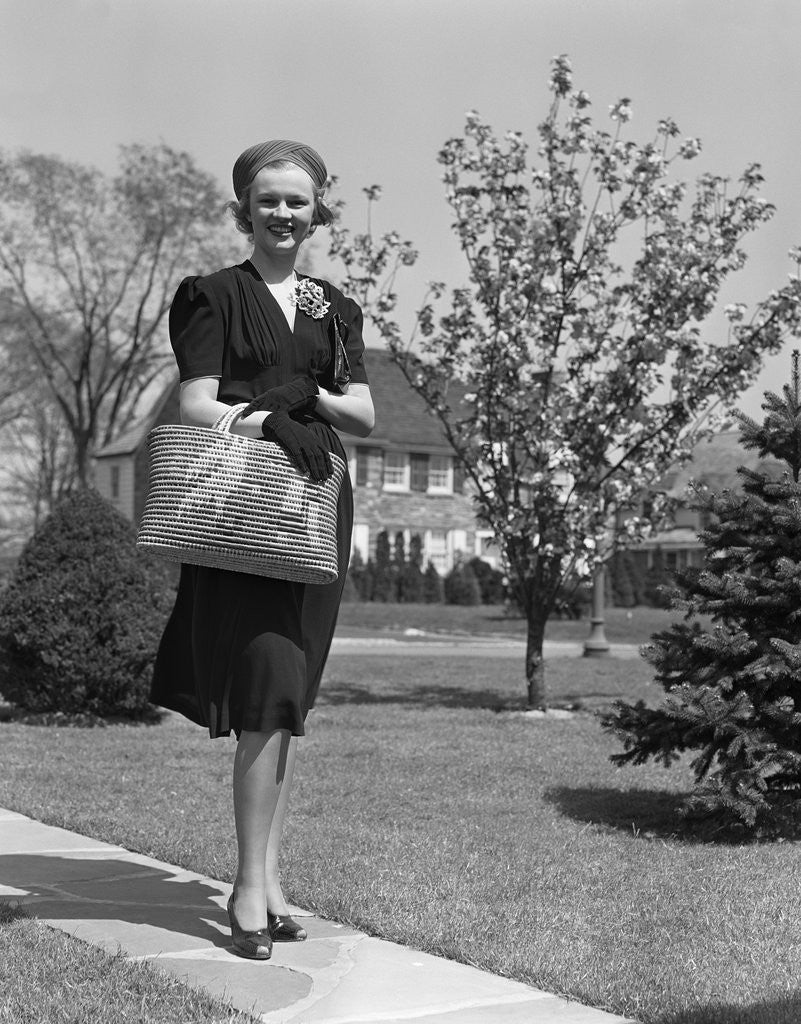Detail of Stylishly dressed woman walking down suburban street carrying straw bag by Anonymous