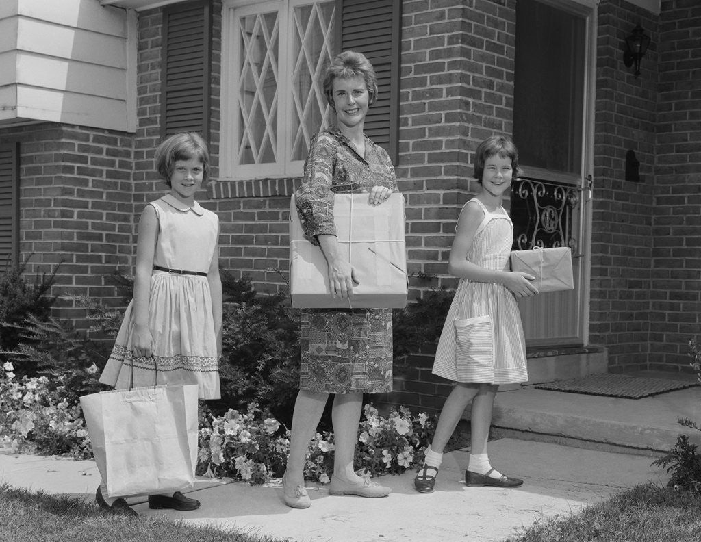 Detail of Mother and two daughters carrying shopping bags packages into house by Corbis