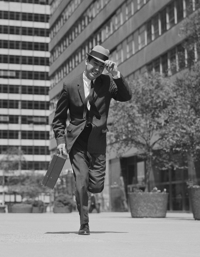 Detail of Businessman carrying briefcase holding his hat on running down urban sidewalk by Anonymous