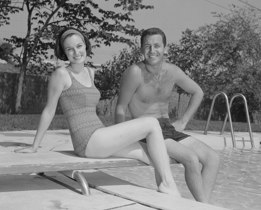 Detail of Man woman couple sitting on diving board on side of swimming pool by Corbis