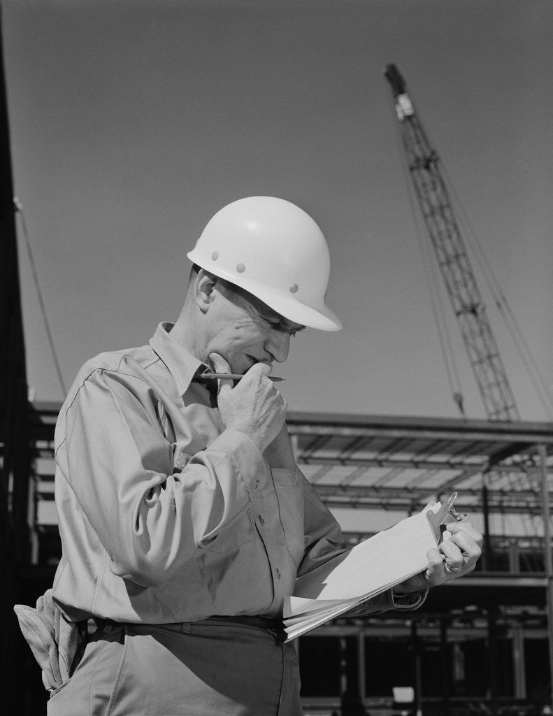Detail of Male construction site supervisor wearing hard hat reading papers by Anonymous