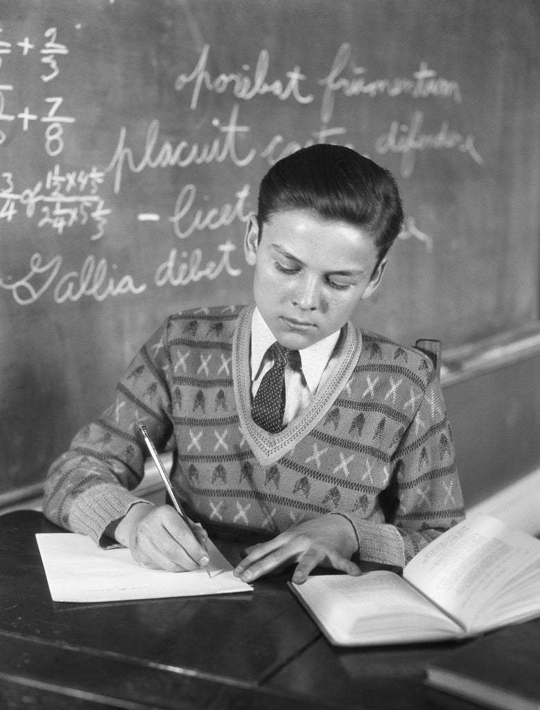Detail of Boy vee neck sweater writing at school desk by Corbis