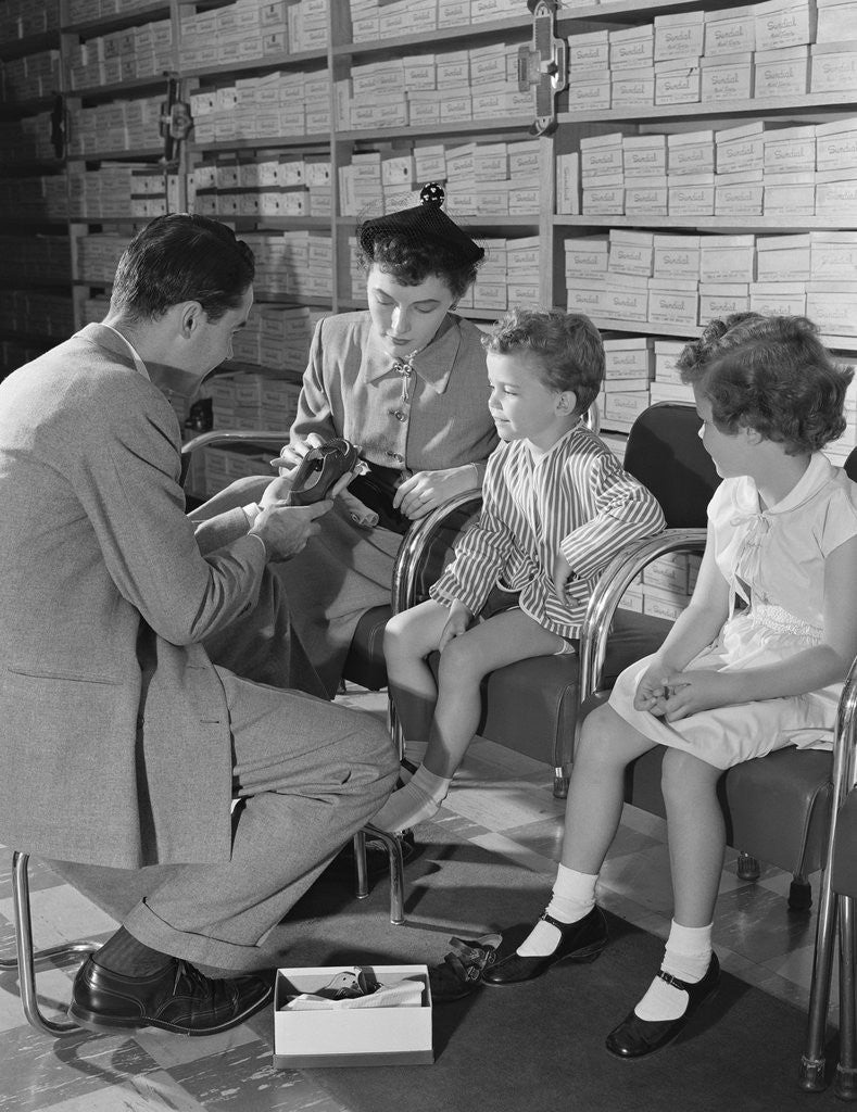 Detail of Family mother two children in shoe store trying new shoes helped by salesman by Anonymous