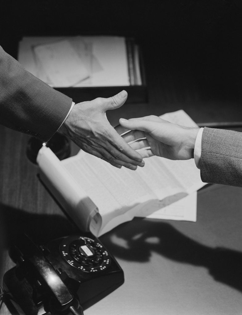 Detail of Close-up two male hands about to shake over desk with papers and telephone by Anonymous