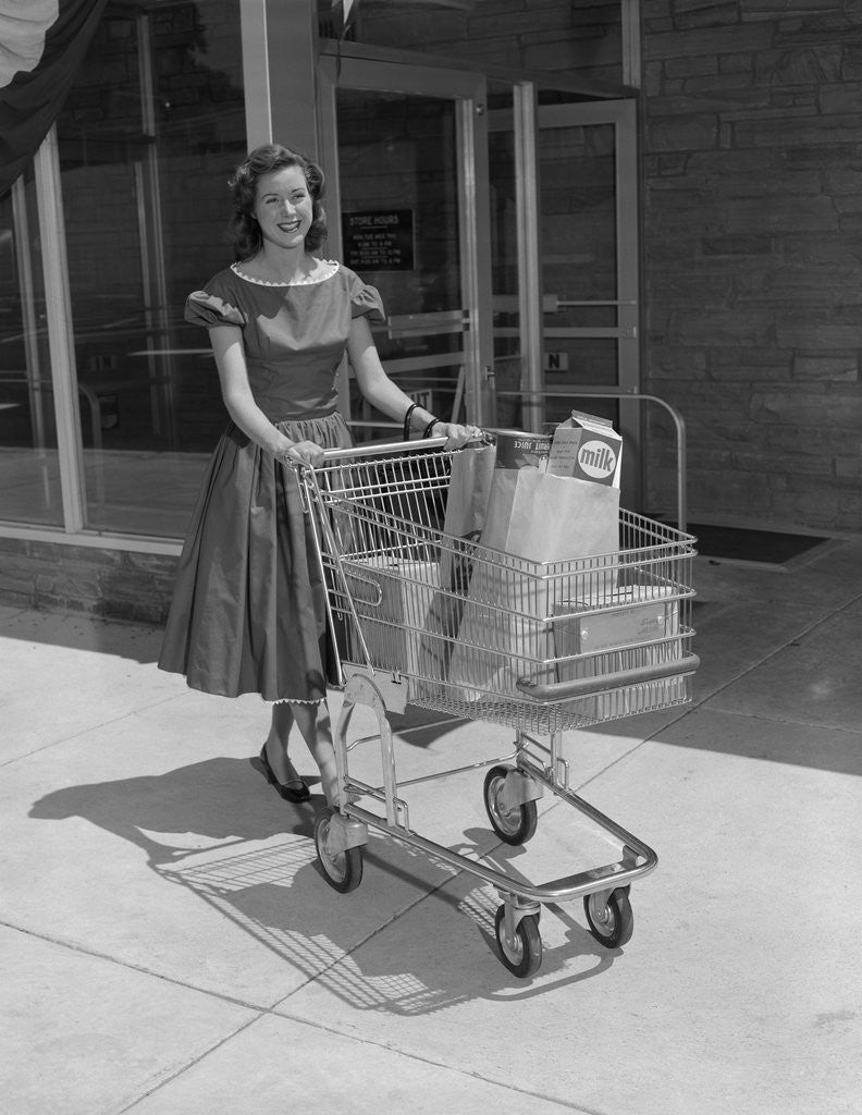 Detail of Smiling woman pushing grocery cart out of supermarket by Corbis