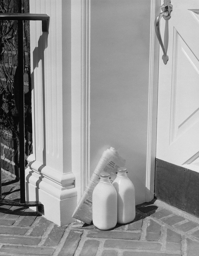 Detail of Glass milk bottles and newspaper by front door home delivery by Anonymous