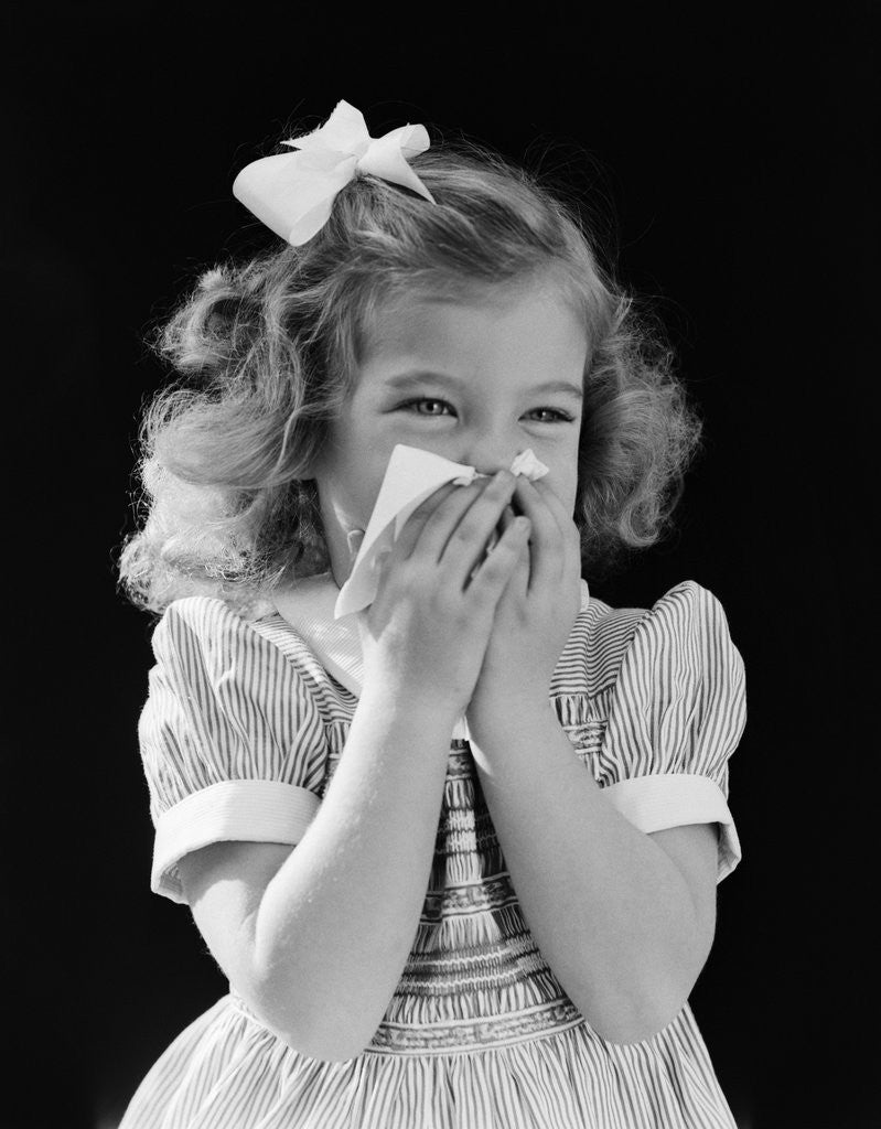 Detail of 1940s little blond girl ribbon in hair holding tissue to nose sneezing by Anonymous