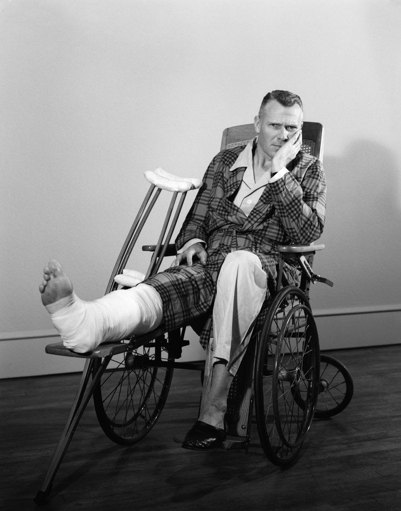 1950s man in wheelchair leg in cast with crutches at side looking at camera by Corbis