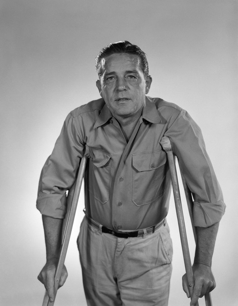 Detail of 1960s man walking on crutches looking at camera by Anonymous