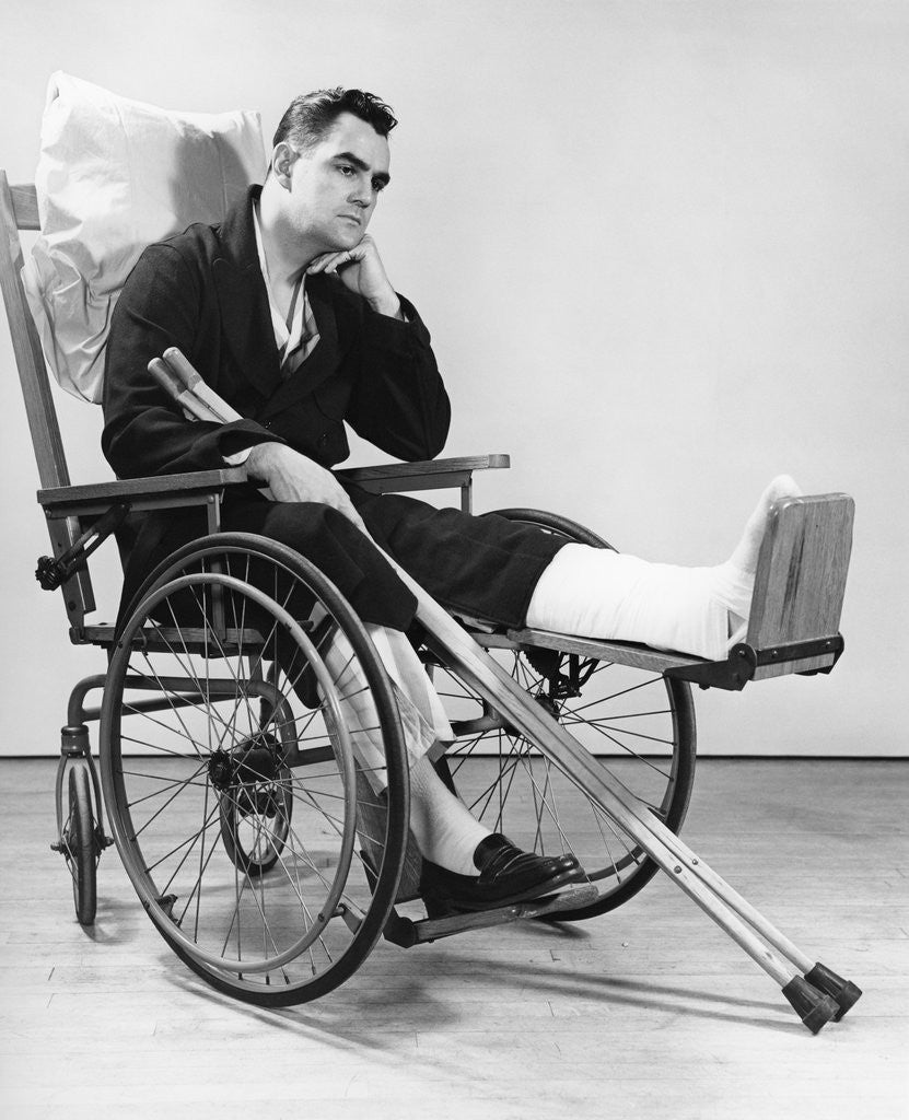 Detail of 1940s man in wheelchair with cast on left leg holding crutches by Anonymous