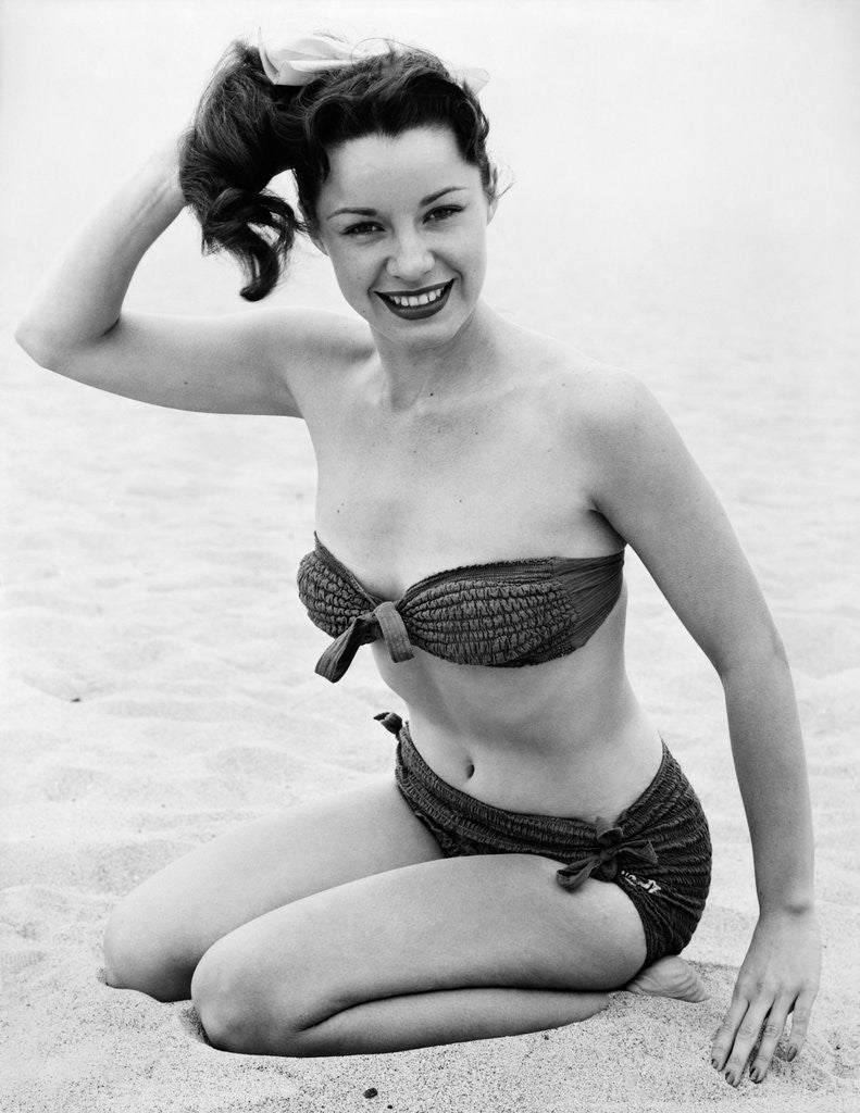 1950s young woman wearing bikini bathing suit kneeling on beach looking at camera posters prints by Corbis