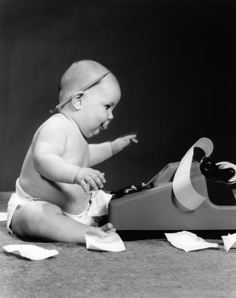Detail of 1960s side view of chubby baby seated behind adding machine with pencil behind ear & tape scattered on floor by Anonymous