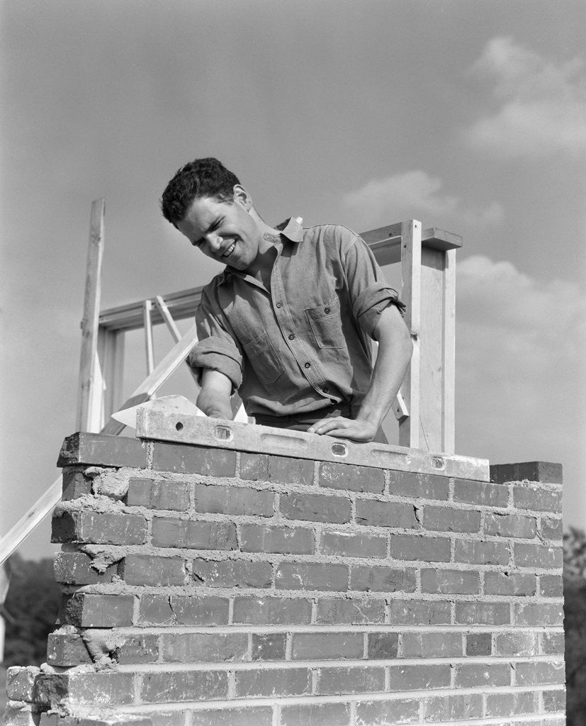 Detail of 1940s man working with level on brick wall chimney construction by Corbis