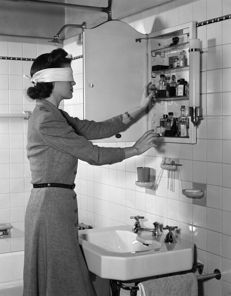 Detail of 1940s woman wearing blindfold reaching into bathroom medicine cabinet by Anonymous