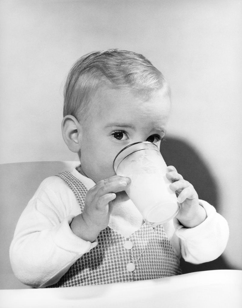 Detail of 1950s boy toddler drinking glass milk looking at camera by Anonymous