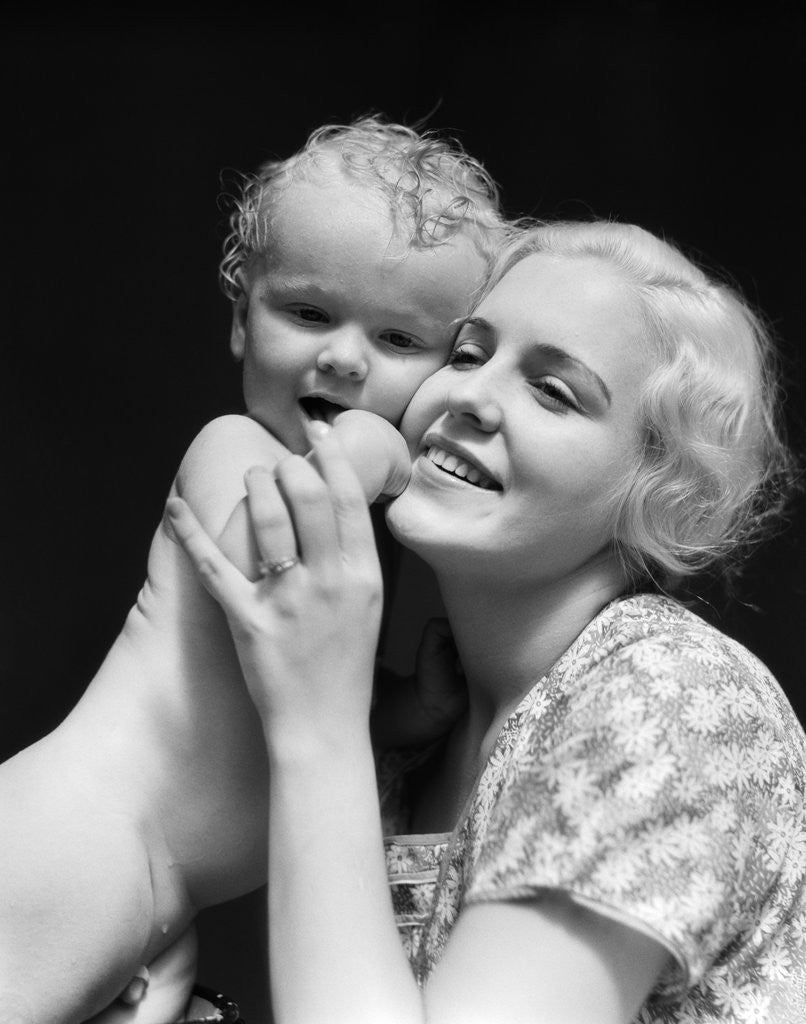 Detail of 1930s blonde woman mother smiling holding baby to cheek by Corbis