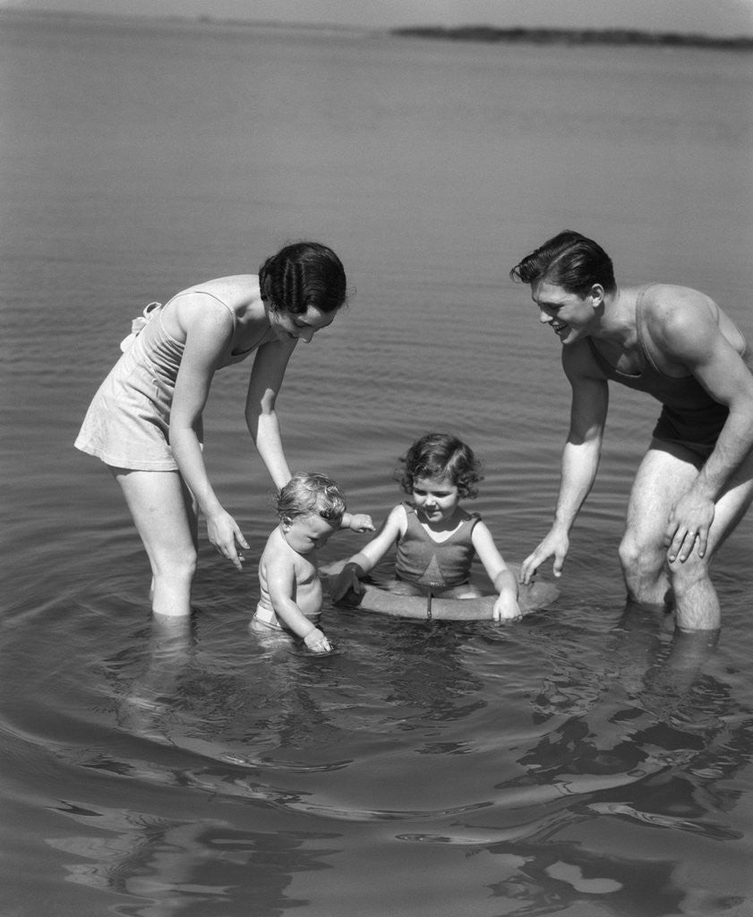 Detail of 1930s family father mother daughter son with rubber inner tube wading in seashore water by Anonymous