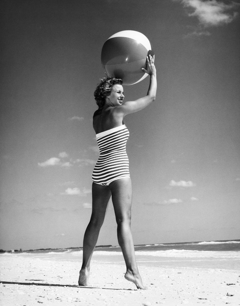 Detail of 1960s woman in stripes swim suit bathing holding beach ball standing on tip toes by Anonymous