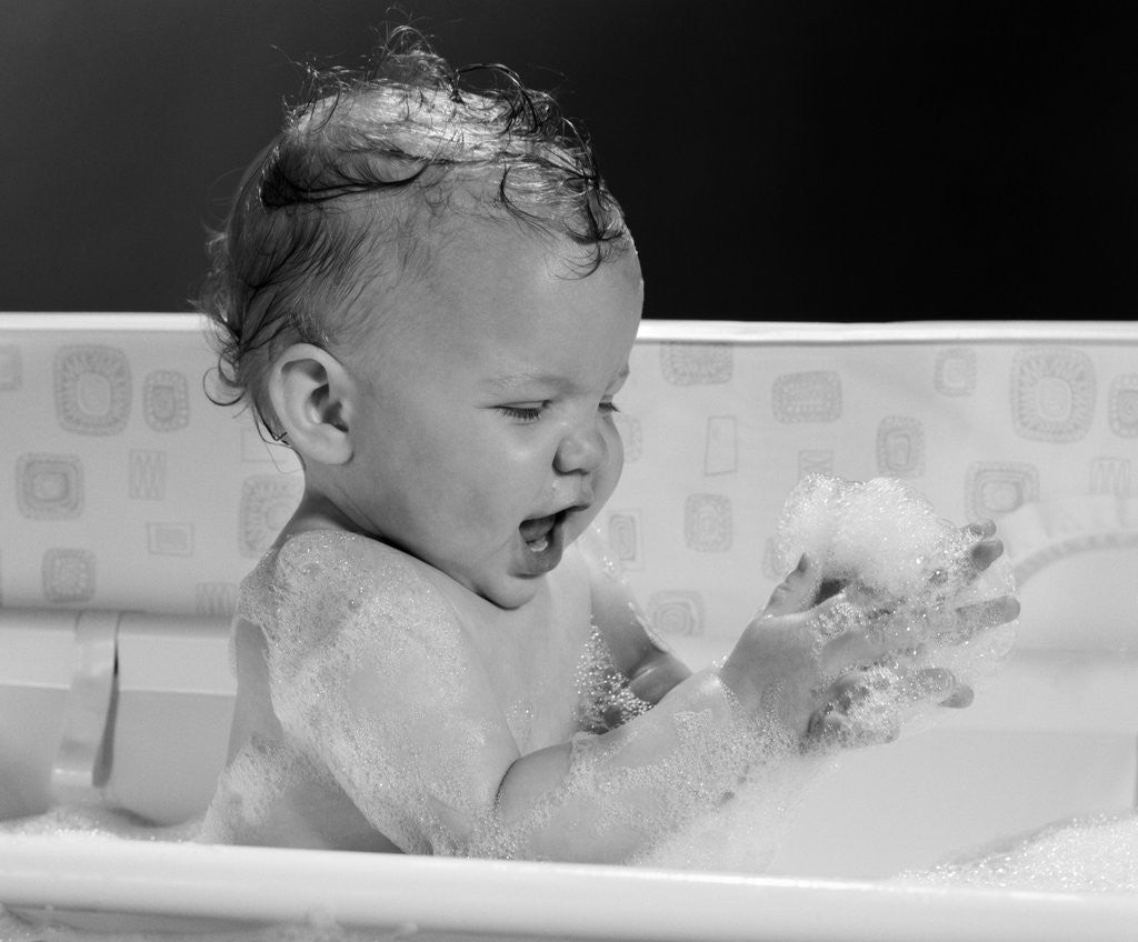 Detail of 1960s baby in bathtub playing with suds indoor by Anonymous