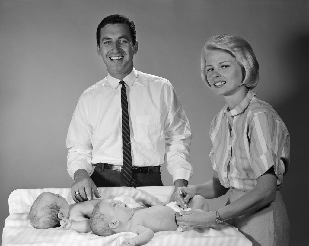 Detail of 1960s smiling mother and father with twin babies on diaper changing table looking at camera by Corbis