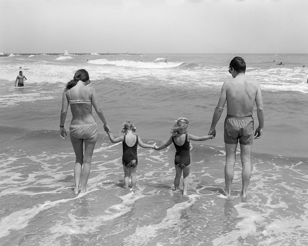 Detail of 1970s family on vacation at ocean beach holding hands walking on sand in surf by Anonymous