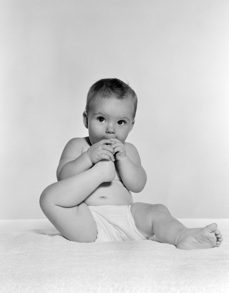 Detail of 1950s 1960s baby seated on blanket bringing foot to mouth by Anonymous