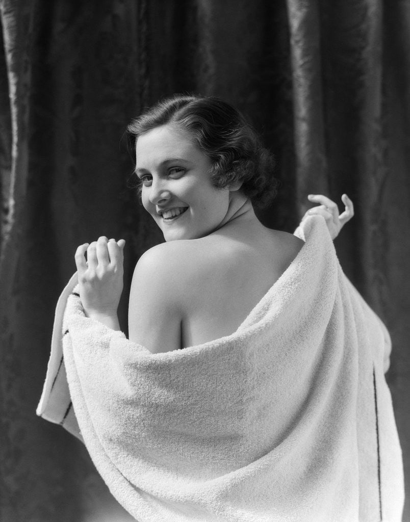 Detail of 1930s smiling brunette woman looking over shoulder drying back with towel looking at camera by Anonymous