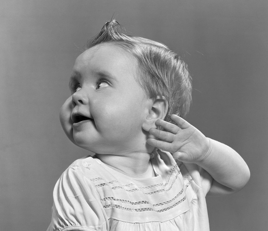 Detail of 1940s 1950s close-up portrait of baby girl with curl on top of head looking to side with hand held up beside ear by Anonymous