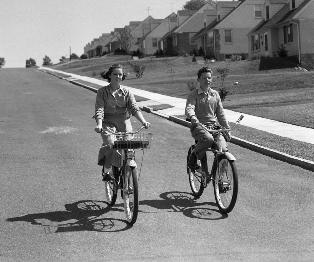 Detail of 1950s teen boy girl couple riding bikes down residential street by Anonymous