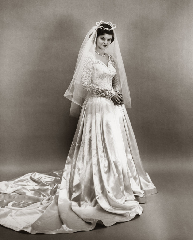 Detail of 1950s full length portrait bride standing wearing satin and lace wedding gown veil and tiara looking at camera by Corbis