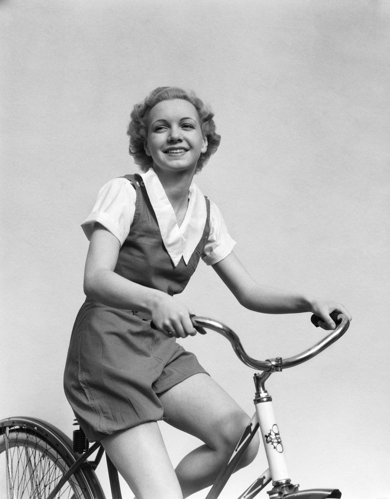 Detail of 1930s smiling blonde woman riding bicycle looking at camera by Corbis