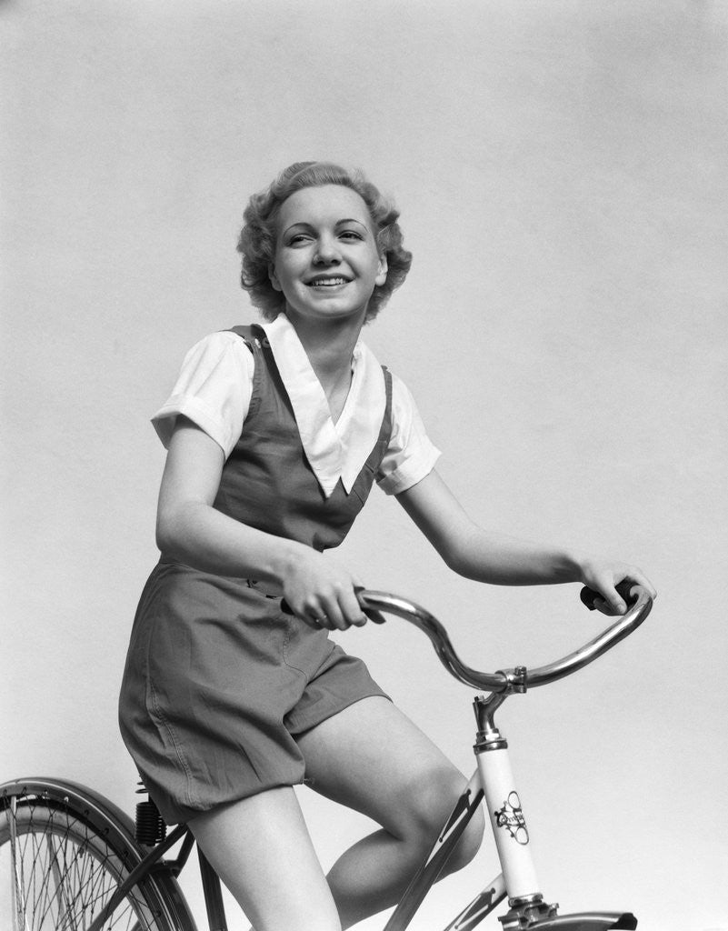 1930s smiling blonde woman riding bicycle looking at camera posters prints by Corbis