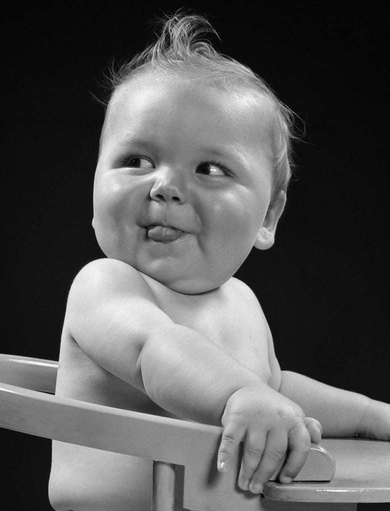 Detail of 1950s 1940s baby in high chair head turned to one side with tongue sticking out funny facial expression by Anonymous