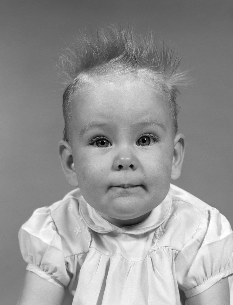 Detail of 1960s head on portrait of baby girl in ruffled dress straight up hair looking at camera by Anonymous