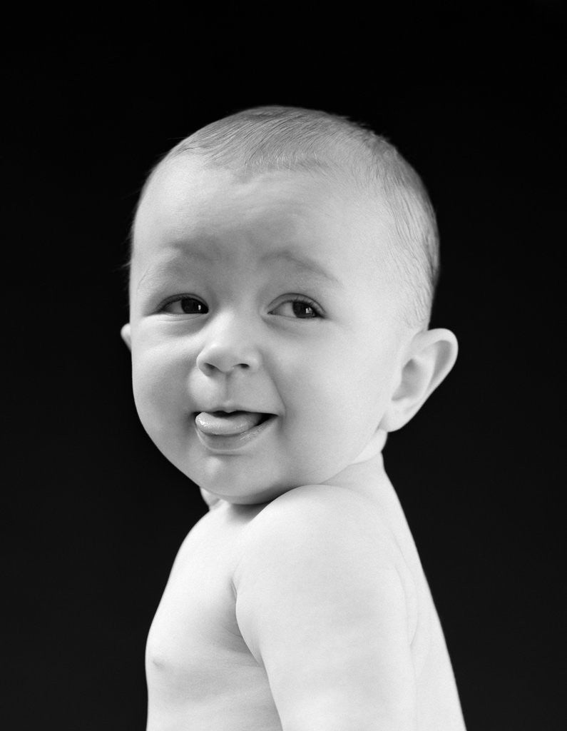 Detail of 1940s 1950s baby head & shoulders smiling sticking out tongue by Corbis